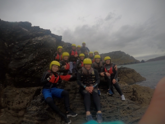 Gente feliz sonriendo y usando cascos amarillos y ayudas de flotabilidad naranjas durante su experiencia de Coasteering 