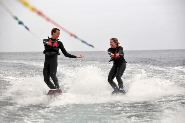  Niño y niña con trajes de neopreno negros y flotadores rojos haciendo wakeboard
