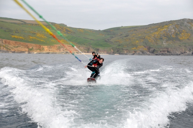 Niño y niña con flotadores rojos y trajes de neopreno negros haciendo wakeboard 