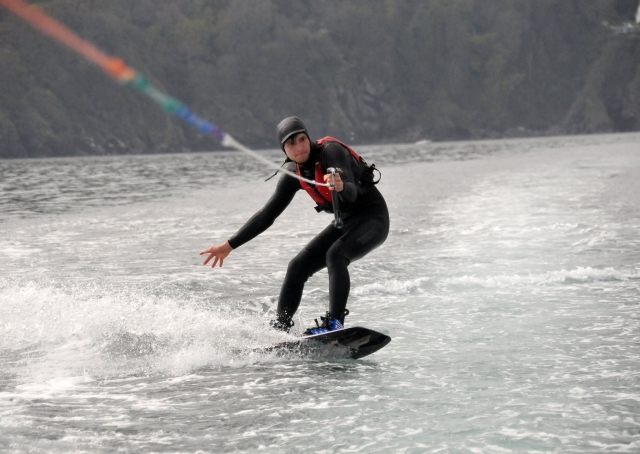  Niño con traje de neopreno negro y flotadores rojos haciendo wakeboard 