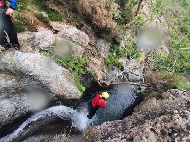  Femme portant un casque jaune et des aides à la flottabilité rouges sautant dans l'eau depuis la falaise