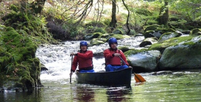 Two boys wearing blue helmets and red buoyancy aids canoeing around the lake