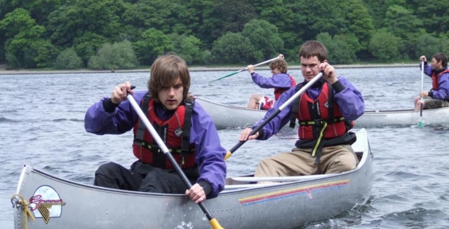 Two groups of people canoeing, wearing red buoyancy aids and having fun canoeing