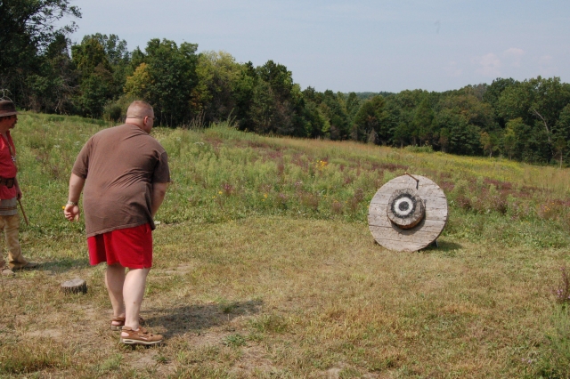 Man in brown t-shirt and red shorts axe throwing