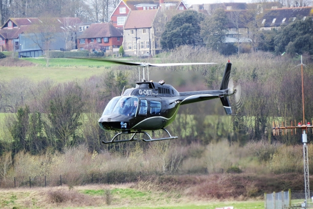  Hombre volando en un helicóptero negro sobre el bosque y el pueblo al fondo 