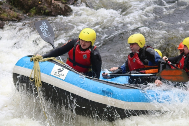  Familie mit ihrem Kind mit gelben Helmen und roten Schwimmhilfen beim Rafting auf dem Fluss 