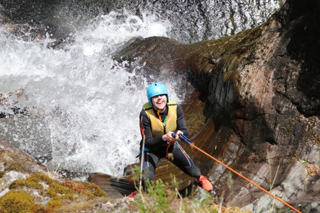  Ragazzo sorridente, che indossa il casco blu, gli aiuti al galleggiamento gialli e si arrampica