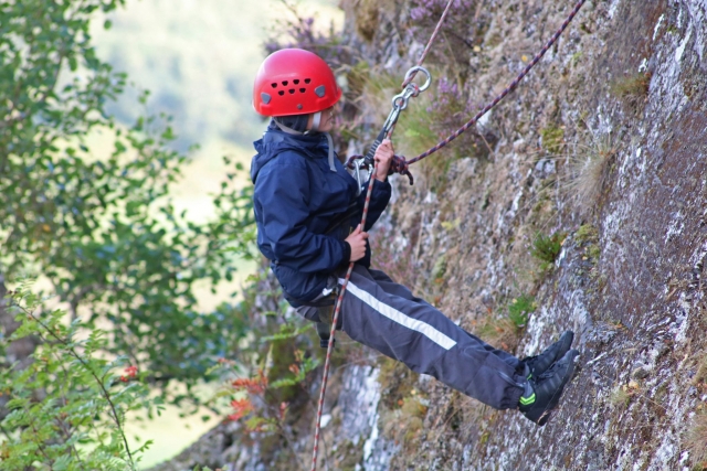 Un ragazzino che indossa un casco rosso si arrampica per la prima volta su roccia 