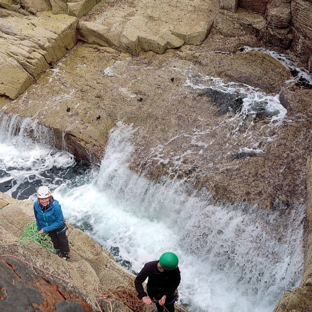 Woman wearing white helmet, blue jacket, smiling and canyoning