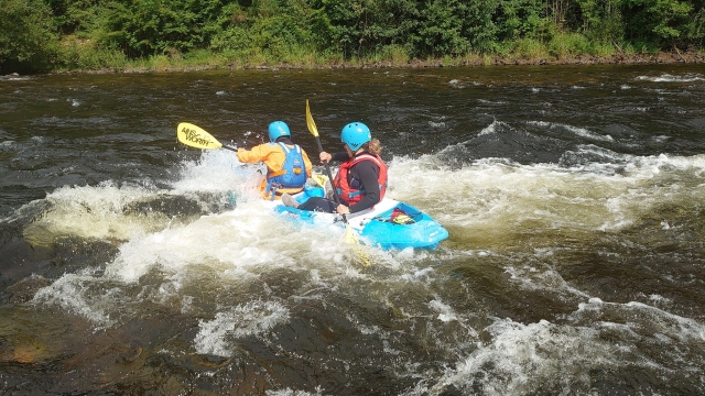 Two young girls wearing red buoyancy aids and helmets kayaking
