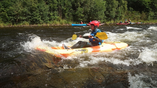 Young boy wearing red helmet and blue buoyany aids kayaking