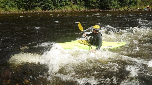 Young boy wearing yellow helmet and black wetsuit kayaking