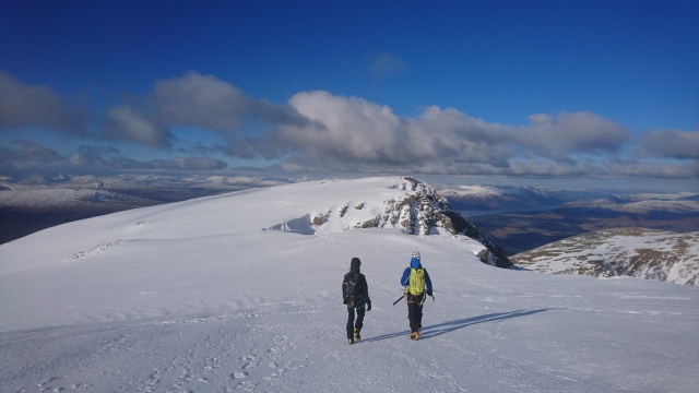 Avventuriero con giacca blu e zaino che scala il Ben Nevis con l'istruttore 