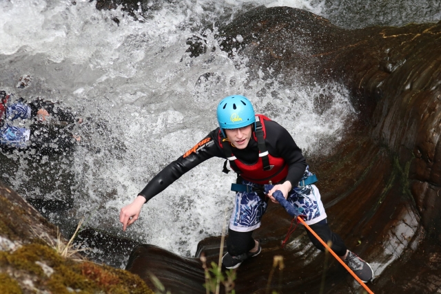  Junge klettert die Wasserfälle hinauf und trägt blauen Helm und rote Schwimmhilfen 