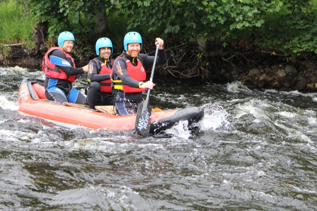 Trois hommes portant des casques bleus et des aides à la flottabilité rouges naviguant sur la partie agitée de l'eau pendant leur séance de rafting 