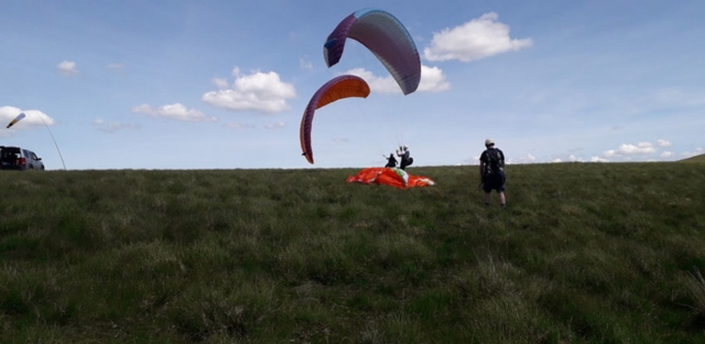 Dos personas a punto de hacer parapente usando parapentes azules y naranjas 