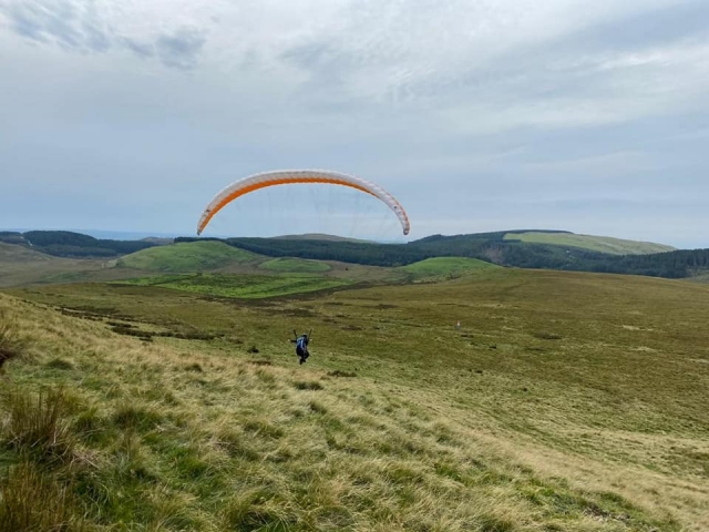  Aventurero volando con parapentes naranjas y montañas alrededor 
