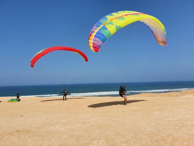 Tres personas aterrizando en la playa después de un parapente Sesión con parapente amarillo y rojo.