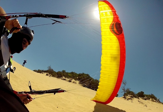  Gelb-roter Motorschirm, der von einem Mann mit schwarzem Helm benutzt wird und vom Strand abhebt 