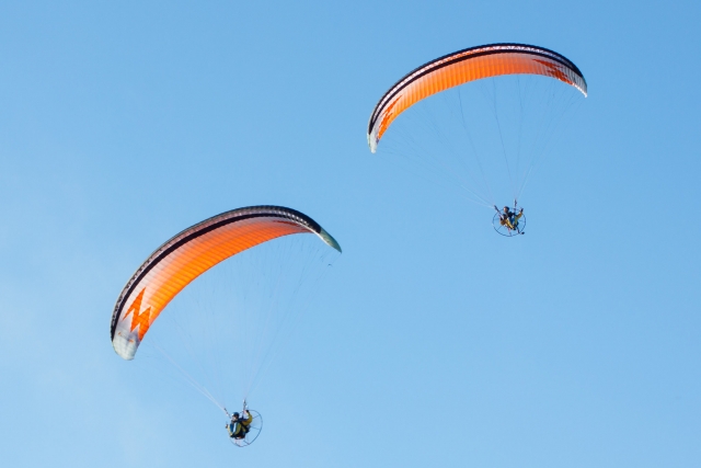 Zwei Personen genießen ihr Gleitschirmerlebnis und fliegen mit orangefarbenen Motorschirmen 