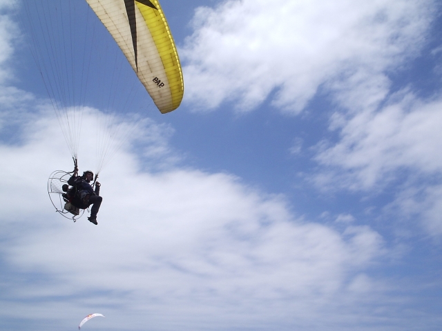 Junge mit Gurtzeug und schwarzem Helm fliegt mit weißem und gelbem Motorschirm 