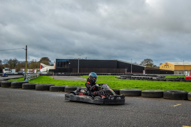  Fille portant un casque bleu et une combinaison de conduite noire de karting et des installations à l'arrière 