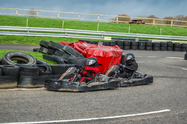  Deux personnes, l'une portant une combinaison de conduite rouge et un casque noir et l'autre, casque noir et combinaison de conduite, karting 