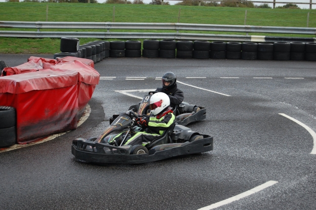  Conductor con traje de conducción verde y negro y casco negro y otro conductor con casco y traje de conducción, todos de negro, durante su Carrera de Karting Grand Prix 