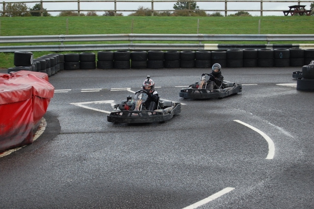  Dos personas con cascos rojos y negros y trajes de conducción compitiendo y divirtiéndose con su carrera de Karting Grand Prix 