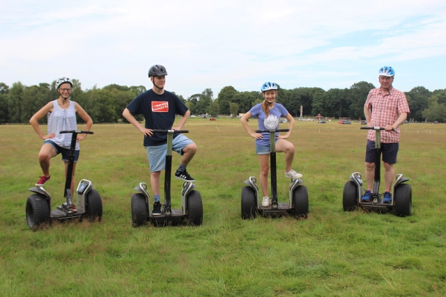 Family of four wearing blue helmets striking a pose, smiling and having fun during their segway journey in the park