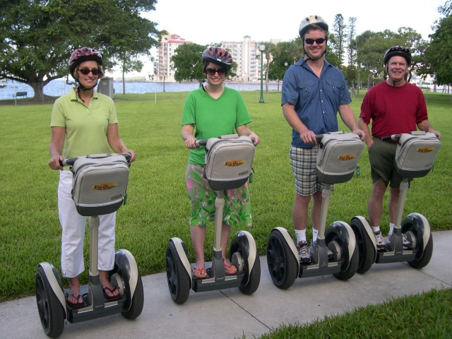  Dos mujeres y dos hombres sonriendo, usando cascos negros durante su sesión de segway