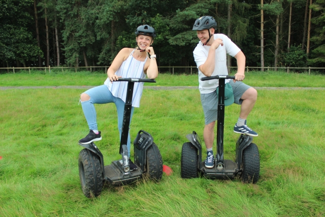  Dos amigos vistiendo camisetas blancas y cascos negros disfrutando de su fin de semana haciendo segway en el parque