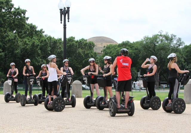People wearing white helmets getting ready to ride segways around the park 
