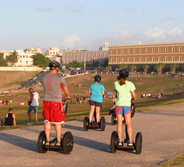 Family of three wearing black helmets and doing segway around the park