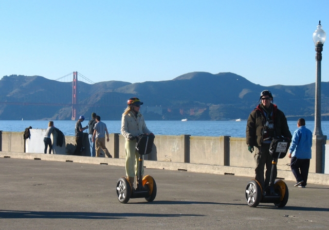 Boy and girl wearing black helmets during their segway adventure around the park and sea at the back