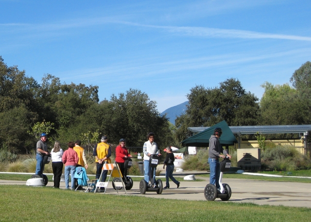  Gruppo di persone che indossano magliette rosse, arancioni e gialle durante la loro avventura in segway nel parco e al lago 