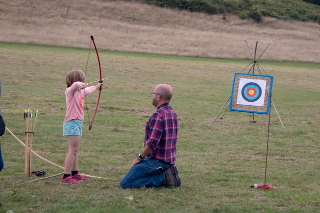 Petite fille portant un t-shirt rose et un short bleu faisant du tir à l'arc avec un instructeur juste à côté d'elle 