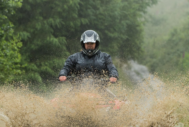  Donna che indossa un casco nero e una giacca che guida il quad sul fiume 