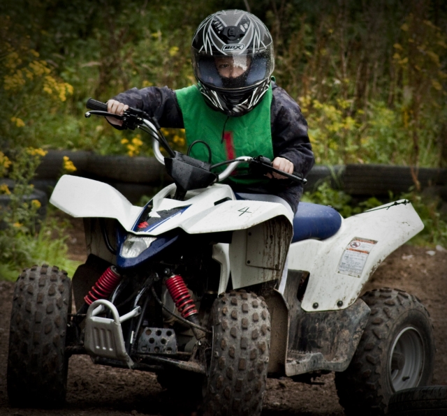  Petit garçon en combinaison de conduite verte et casque noir conduisant un quad autour de la forêt
