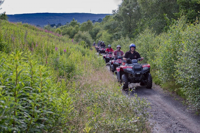 Instructor con casco azul y, detrás de él, un grupo de niños con casco y conduciendo quads rojos por el bosque 