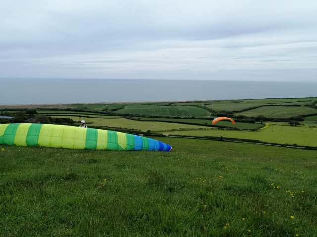 Deux personnes portant des casques blancs et se préparant à voler avec des parapentes orange et vert 
