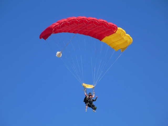 Couple flying above the beach using red and yellow paraglider