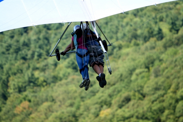 Boy and girl flying over the forest using a white paraglider