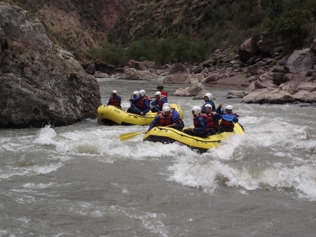  Due gruppi che indossano caschi bianchi, aiuti al galleggiamento rossi e muta blu fanno rafting su barca gialla 