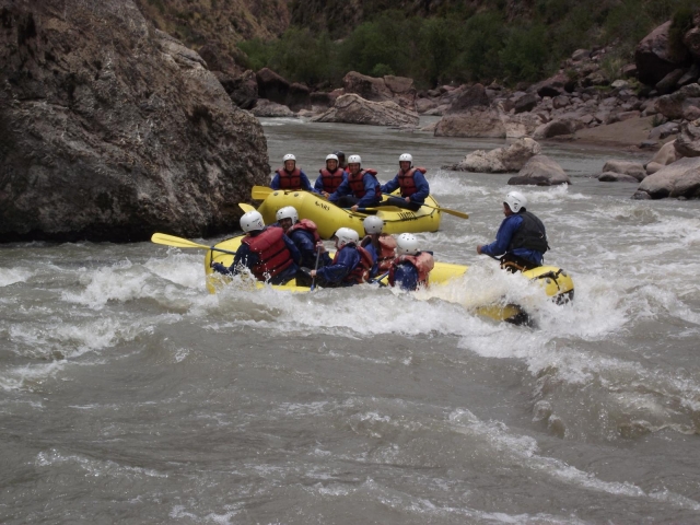 Persone che indossano casco bianco, aiuti al galleggiamento rossi, muta blu e fanno rafting su barca gialla 